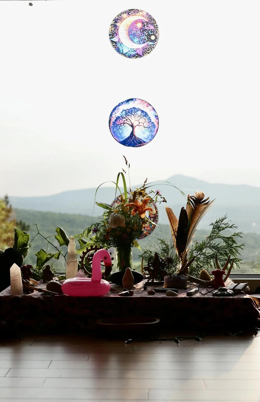 Autel décoré de fleurs et d’objets devant une fenêtre avec vue sur les montagnes.